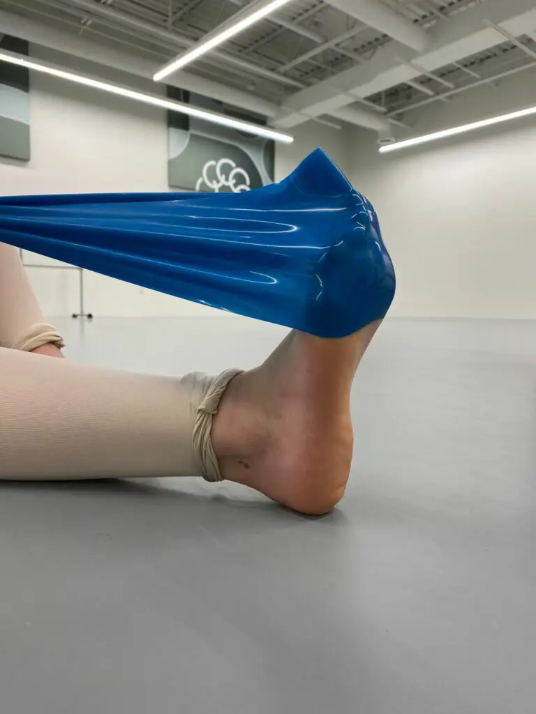 A TheraBand exercise, where a ballerina dancer points her foot on a 90 degree angle with the TheraBand covering the top half of the foot.